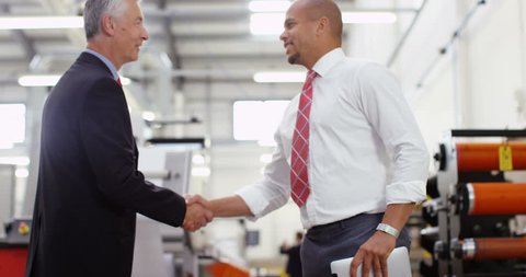 4K Businessmen greet each other & shake hands on the factory floor, looking at computer tablet & discussing operations