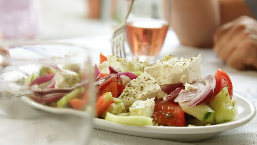 Table setting in restaurant with Greek salad and wine
