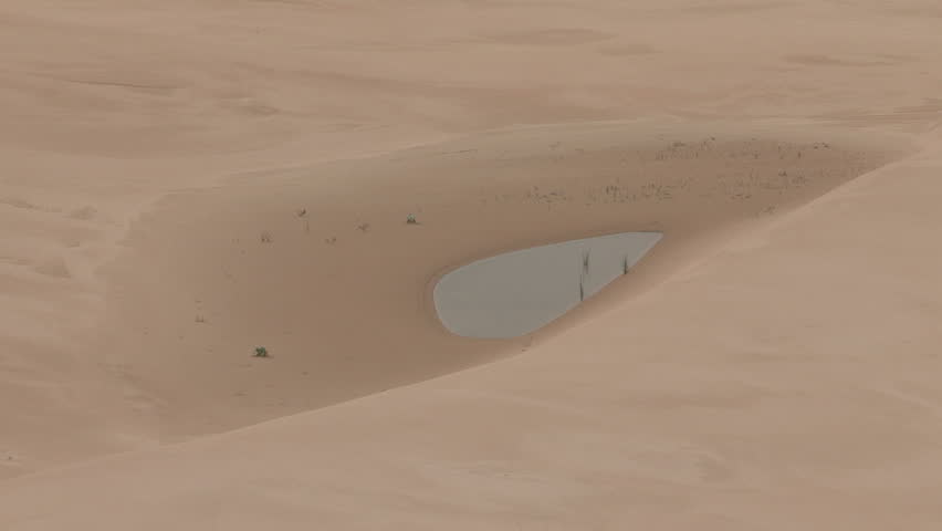 Wide and close up of desert dunes with small pool of water in the middle