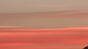 Airplane flying across the frame leaving contrail on an orange sky