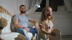 Close-up of father and daughter playing together. Happy little girl is riding a rocking horse and laughing with father smiling and sitting on the big white sofa. - Powered by Shutterstock - Get 15% off with code: PIKWIZARD15