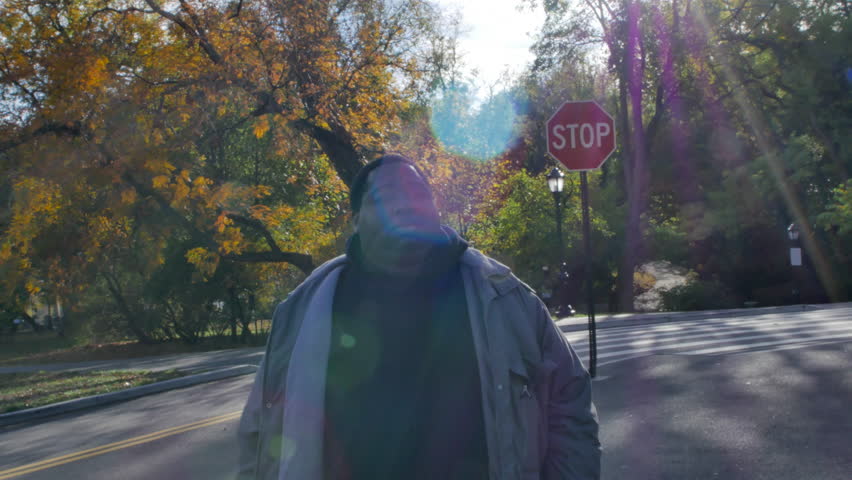 A Man Stands in front of a Stop Sign at the Entrance to a Park on a Bright Fall Day