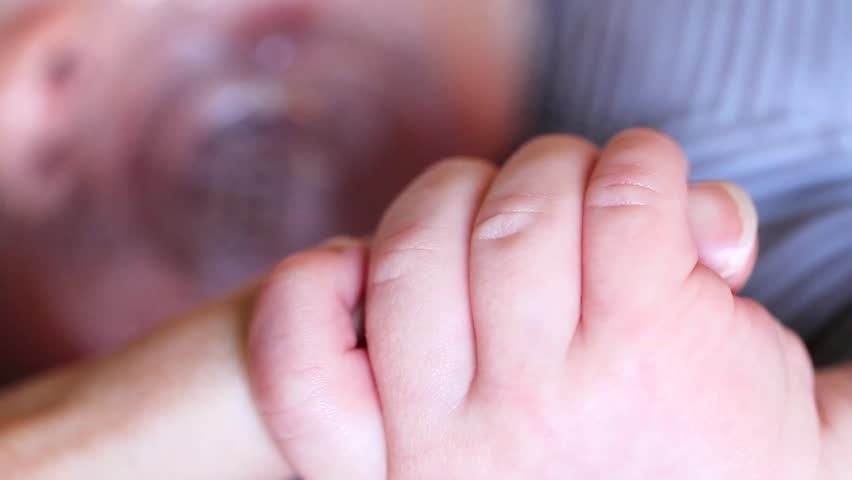 A newborn baby holding his mothers finger