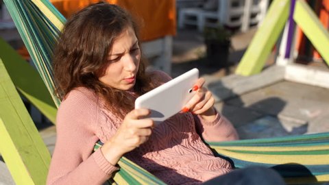 Excited girl lying in hammock and having fun while playing game on tablet
