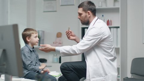 Male Doctor Checks Young Boys Throat. Nurse is Busy in the Background.  