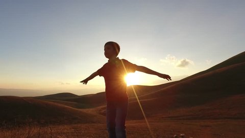 Kid silouette spreading arms and looking to the infinite at the sunset. Conceptual footage.
