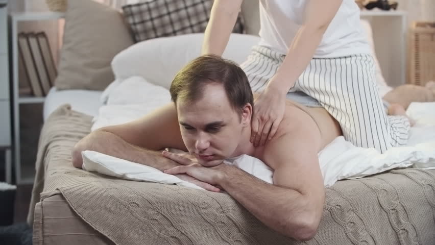 PAN of young woman sitting on top of husband and rubbing his sore shoulders