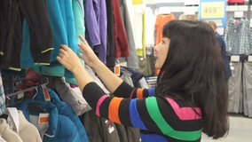 Woman Shopping for Clothing. Young women carefully picking up clothes. Pretty girl doing shopping at clothes store.