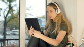 Girl wearing headphones and watching funny video on tablet
