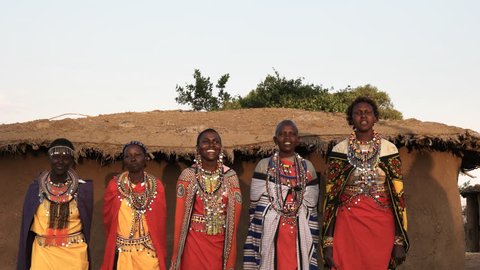 wide shot of five maasai women in traditional dress singing and dancing in a village near maasai mara, kenya