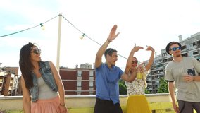 Group of four cheerful friends dancing on the rooftop terrace on sunny day