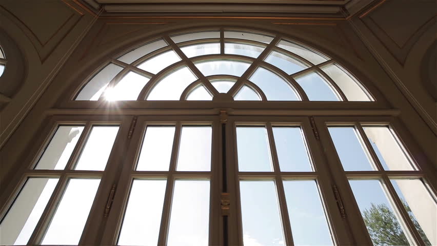 Window view to rural landscape outside with sun beam in glass tracking pan. View from large arch window of French or Italian luxury villa to scenery valley panorama with green trees and hills far away