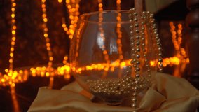 Dark wall and floor decorated with yellow christmas lights. Golden beads in a glass vase.