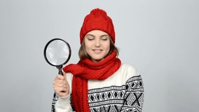 Searching winter woman. Girl wearing warm winter red knitted hat and scarf looking through magnifying glass at blank copy spaces at side and contemplating at the end, studio shot