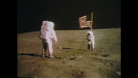 UNITED STATES: 1970s: Men on moon salute USA flag. Astronauts walk on moon