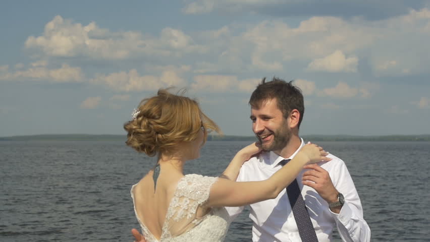 The bride and groom are standing on a pier and a kissing