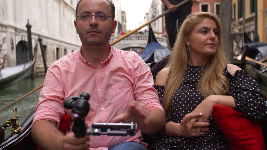 Beautiful lovers couple in Venice on Gondola ride filming from the boat. Romance shot in boat. Happy together on travel vacation holiday in Venice, Italy.