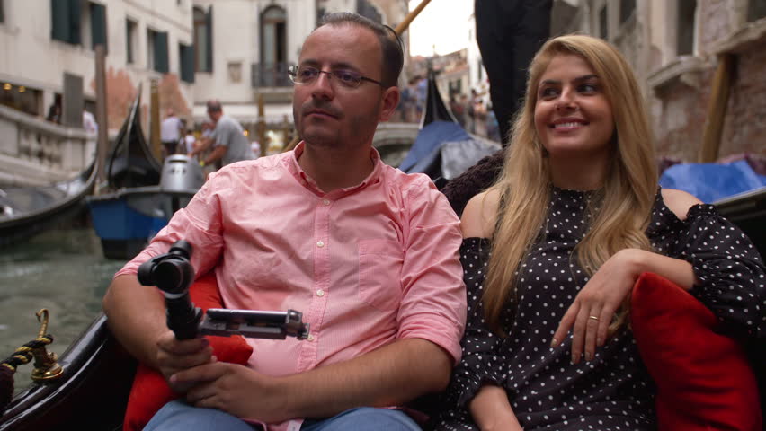 Beautiful lovers couple in Venice on Gondola ride filming from the boat. Romance shot in boat. Happy together on travel vacation holiday in Venice, Italy