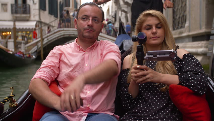 Beautiful lovers couple in Venice on Gondola ride filming from the boat. Romance shot in boat. Happy together on travel vacation holiday in Venice, Italy