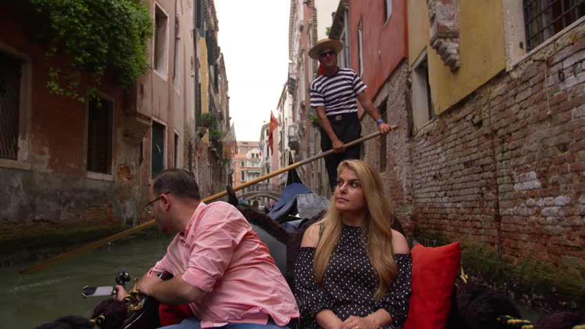 Beautiful lovers couple in Venice on Gondola ride with a gondolier in the background. Romance shot in boat. Happy together on travel vacation holiday in Venice, Italy