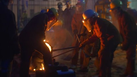 Group of Men is Working Together, Sparks Are Flying. Metallurgists Work at High Temperatures Festival. Workers Are Casting Metal, Pouring Out Into it in Evening, Casting Workshop Outdoors. People
