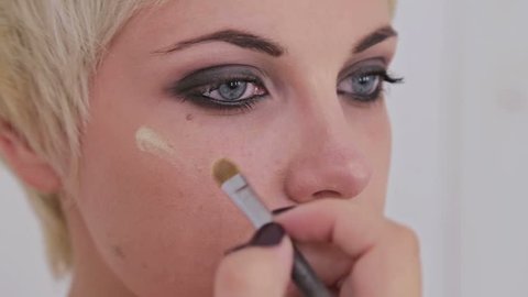 Makeup artist applying liquid tonal foundation on the face of the woman in white make up room. Beauty and fashion concept