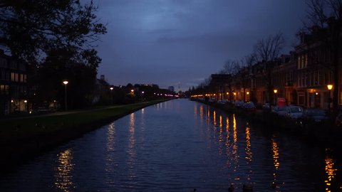 Beautiful shot of Amsterdam canal at Evening with grey mystic clouds and illuminated streets. Light reflects in water. Beautiful background