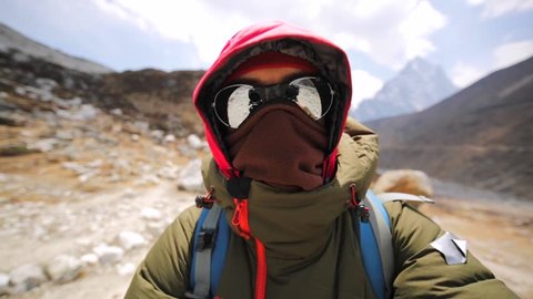Man in sunglasses and warm clothes is making selfie while walking along the Dingboche-Lobuche path in Khumbu valley, mountains of Nepal. Ama Dablam peak is on the background