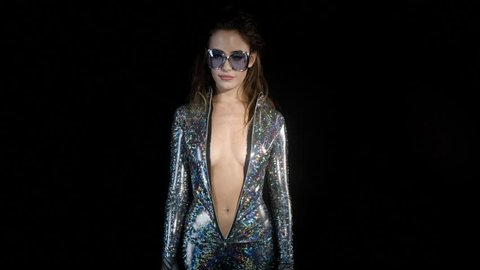 sexy cool woman posing and dancing in a sparkling metallic catsuit with the zip open to her belly, in a disco setting