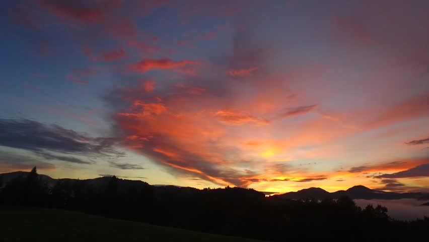 Intensive, bold colors of sunset over dark hills and forests, mountains far away. Some fog, a lot of shadows and silhouettes.