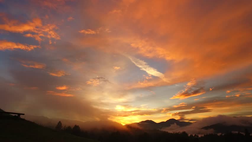 Intensive, bold colors of sunset over dark hills and forests, mountains far away. Some fog, a lot of shadows and silhouettes.