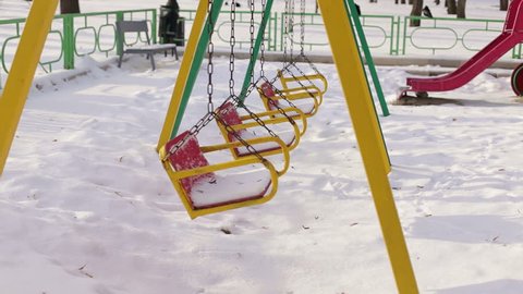 Snow on swing seat in a children's playground. Children's swing in park covered by snow, in winter. Children's swing under a layer of snow.