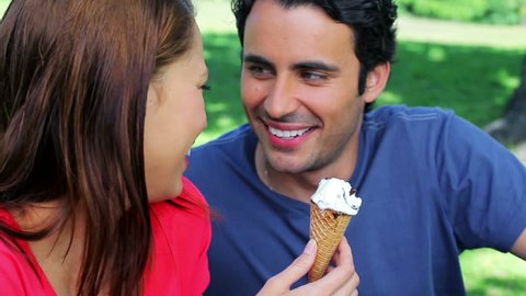 Smiling couple eating ice creams while sitting on the grass in a parkland