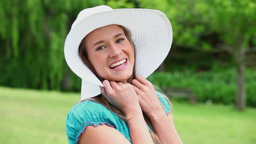 Cheerful young woman holding her hat brim in the countryside