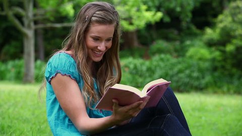 Smiling woman reading a fascinating novel in a park