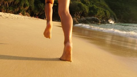 Feet little girls run barefoot on the golden sand beach. Slow motion.