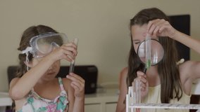 Close up panning shot of girls examining test tubes with magnifying glass / Orem, Utah, United States