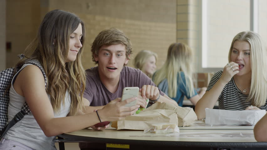 Medium shot of students examining cell phone in school cafeteria / Mapleton, Utah, United States
