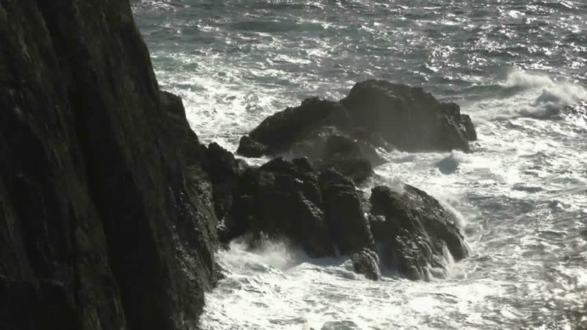 Waves breaking over rocks below lighthouse, a very rugged coastline