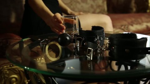 young woman drinking brandy and takes the gag. closeup BDSM accessories and sex toys.