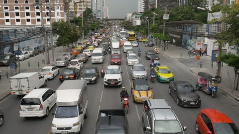 4K Endless traffic jam downtown Bangkok, busy commuter road with cars, tuktuks, motorbikes and colorful taxis, dark grey rainy sky in the background, high angle flyover viewpoint, Southeast Asia
