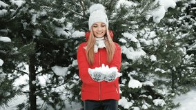 Blonde smiling woman throws snow in winter pine forest outside