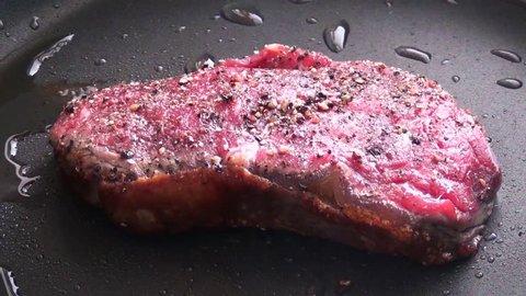 Rump steak with checked peppercorns turned over in a non-stick pan