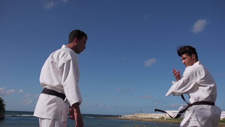 Young people, athletes, sport activity, combat and extreme sports, hispanic men training in karate and traditional martial arts. Simulation of fight on the beach near the sea
