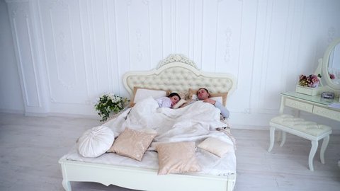 Young Family Sleeping in Morning, Child Woke Up, Jumping on Bed and Want Them to Wake Up. Story Shows White Interior and Beautiful Bed. Concept of Everyday Problems, Family Values.