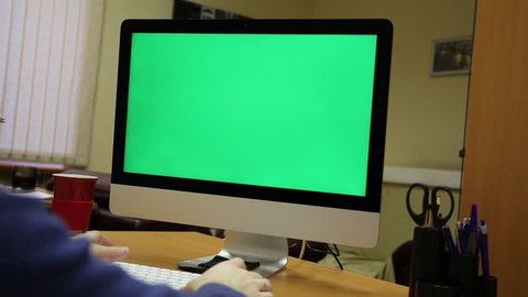 static shot of a man in his home office typing on the keypad in front of a green screen computer display 