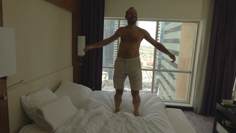 Young, happy man having fun, jumping on bed in room, super slow motion 240fps

