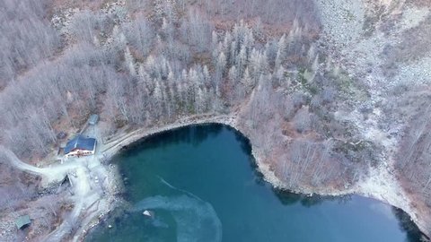 Aerial shot, a beautiful frozen lake in deep blue color, surrounded by frost trees, situated in the middle of the mountains, filmed with drone