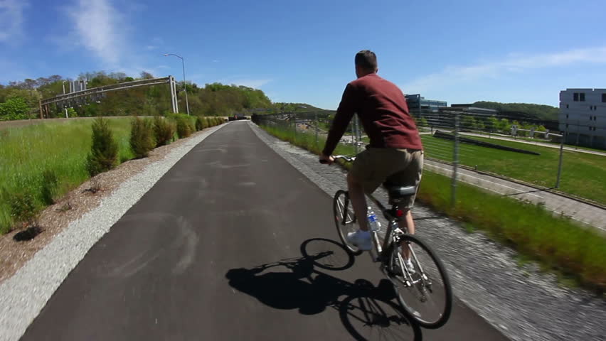 A man rides his bike while standing on a Pittsburgh bike trail.