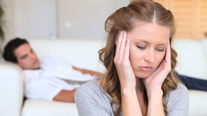 Woman holding her head in her hands as a man sleeps on the couch